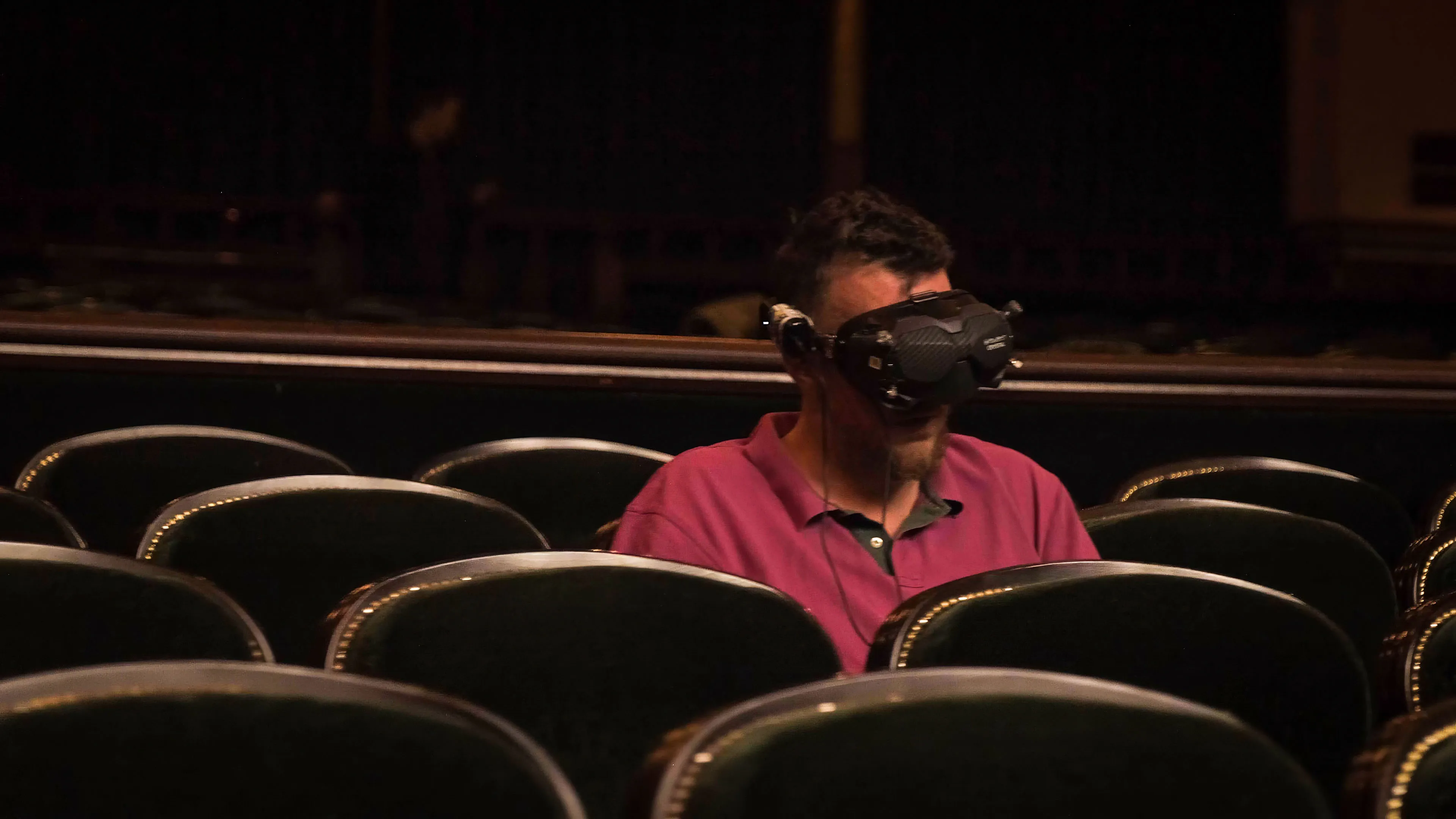 A person wearing a FPV drone headset sits alone in a row of empty theater seats.