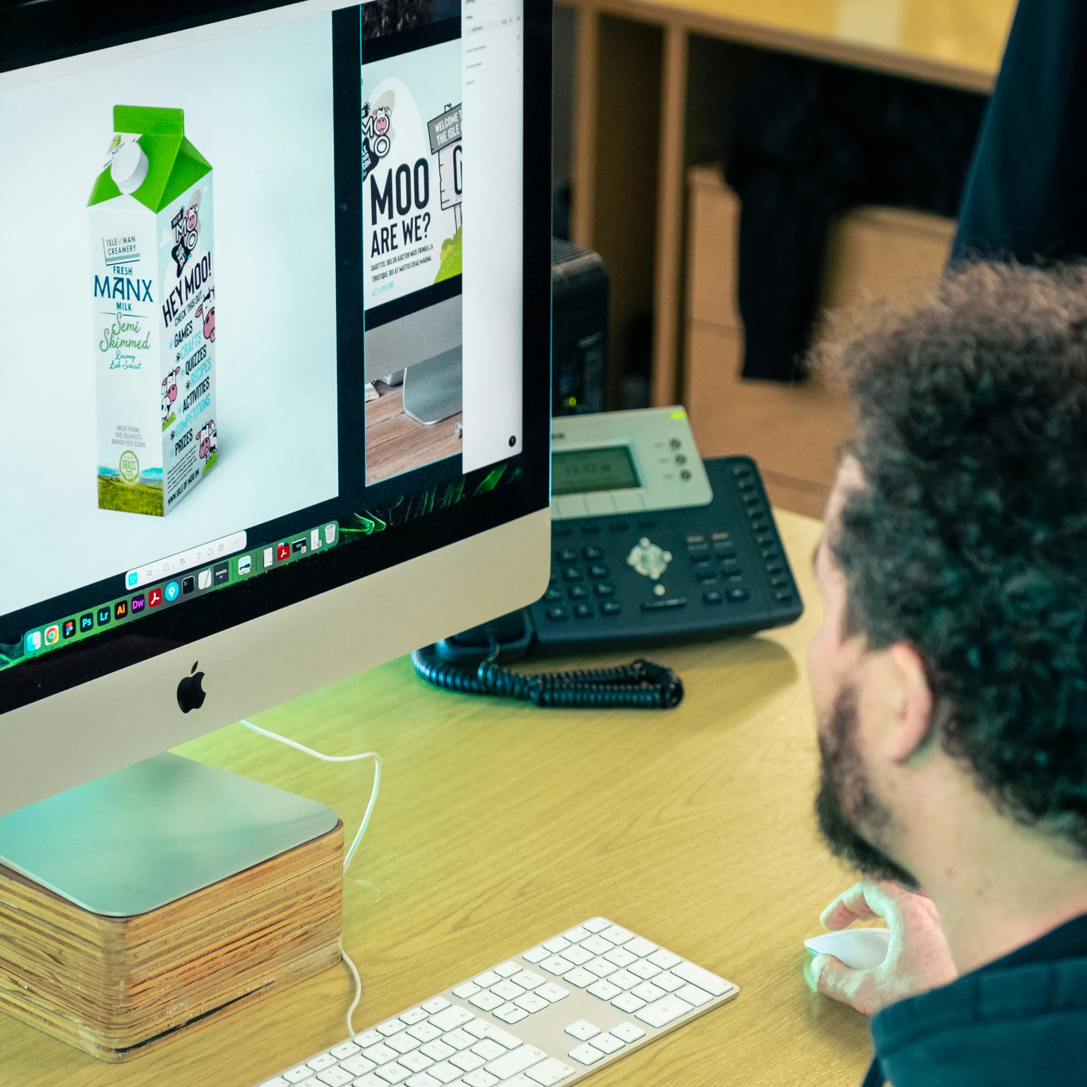 Designer reviewing Isle of Moo milk carton artwork on a desktop computer in a studio setting.